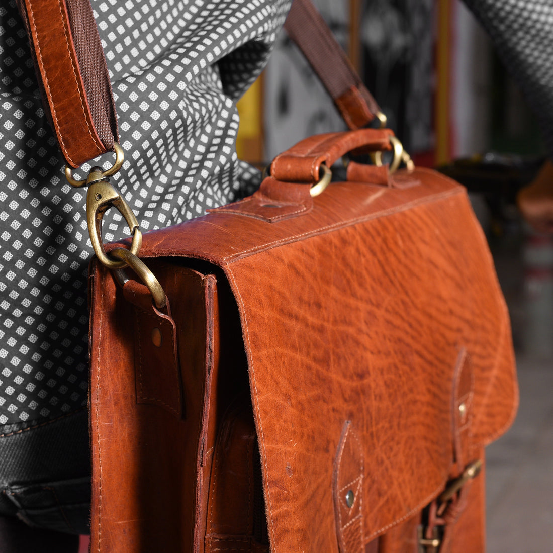 picture of a person walking in a city carring a shoulder bag (brown) looking vintage and used.  