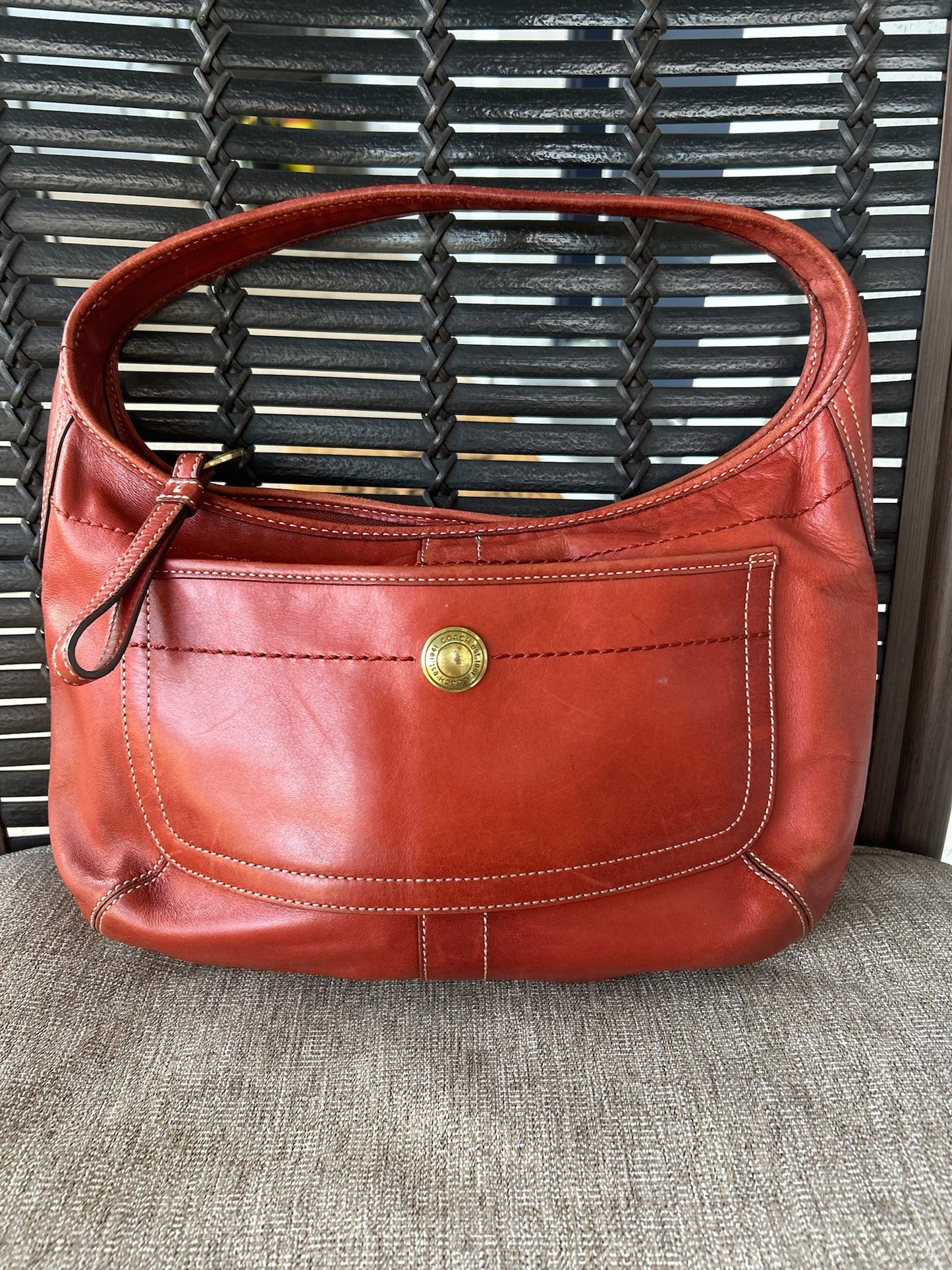 Front view of a Coach hobo bag with a brass button detail, displayed on a lawn chair.