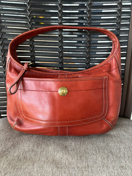 Front view of a Coach hobo bag with a brass button detail, displayed on a lawn chair.